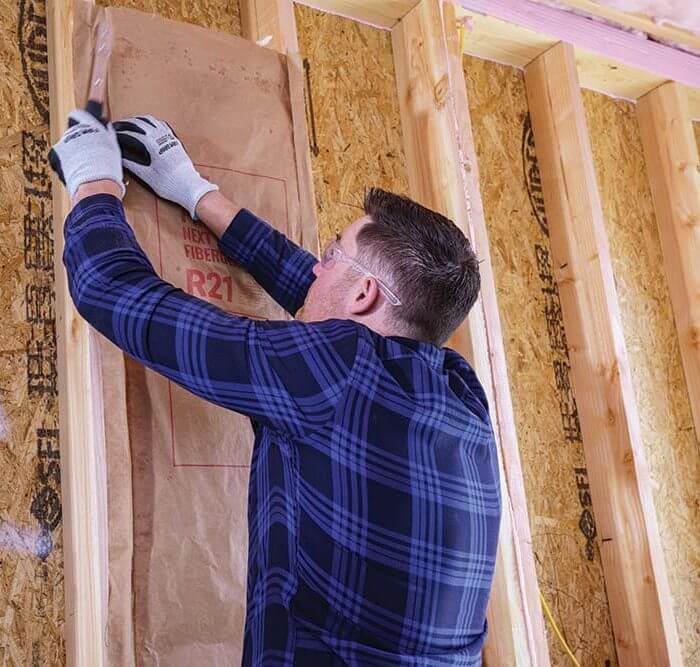 man installing r21 fiberglass on wood frame of wall