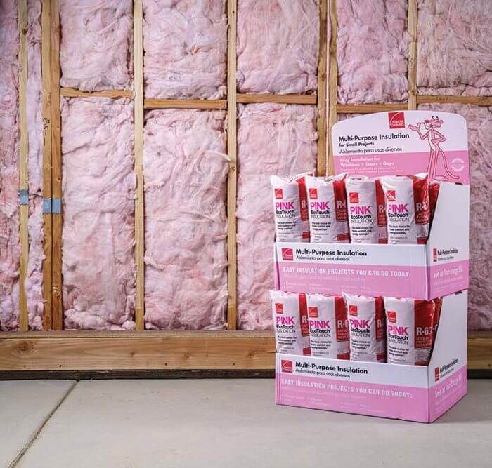 boxes with rolls of pink multipurpose insulation in front of wood frame wall with insulation installed