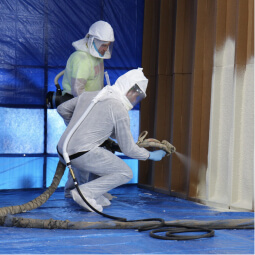 One person demonstrates how to install spray foam insulation while another looks on