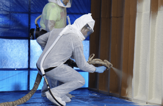 A man in protective equipment spraying foam.