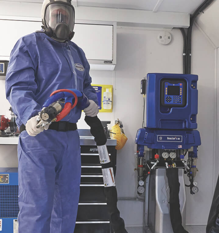 Person in protective gear holds spray foam insulation gun