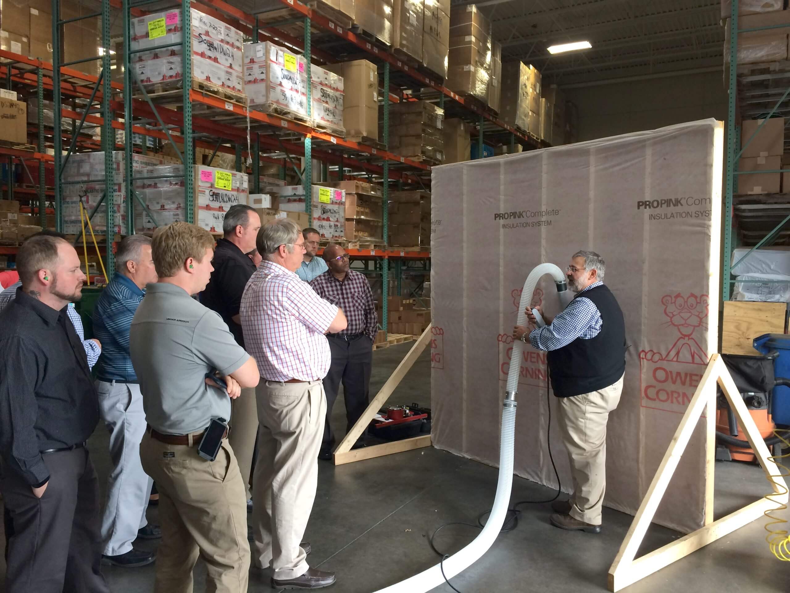 Man demonstrating insulation blowing technique to group of other men