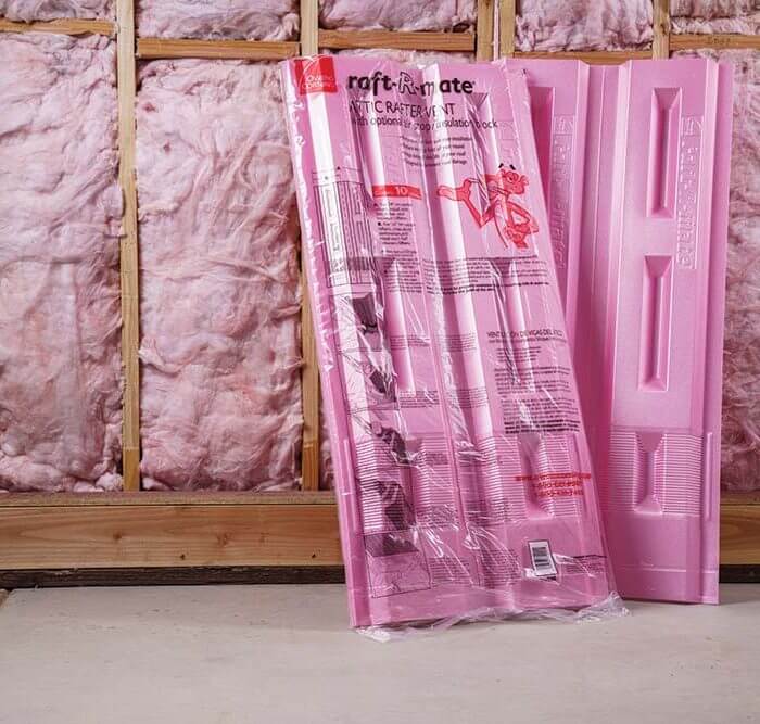 Two packs of pink Owens Corning Raft-R-Mate leaned against a wall with exposed insulation.