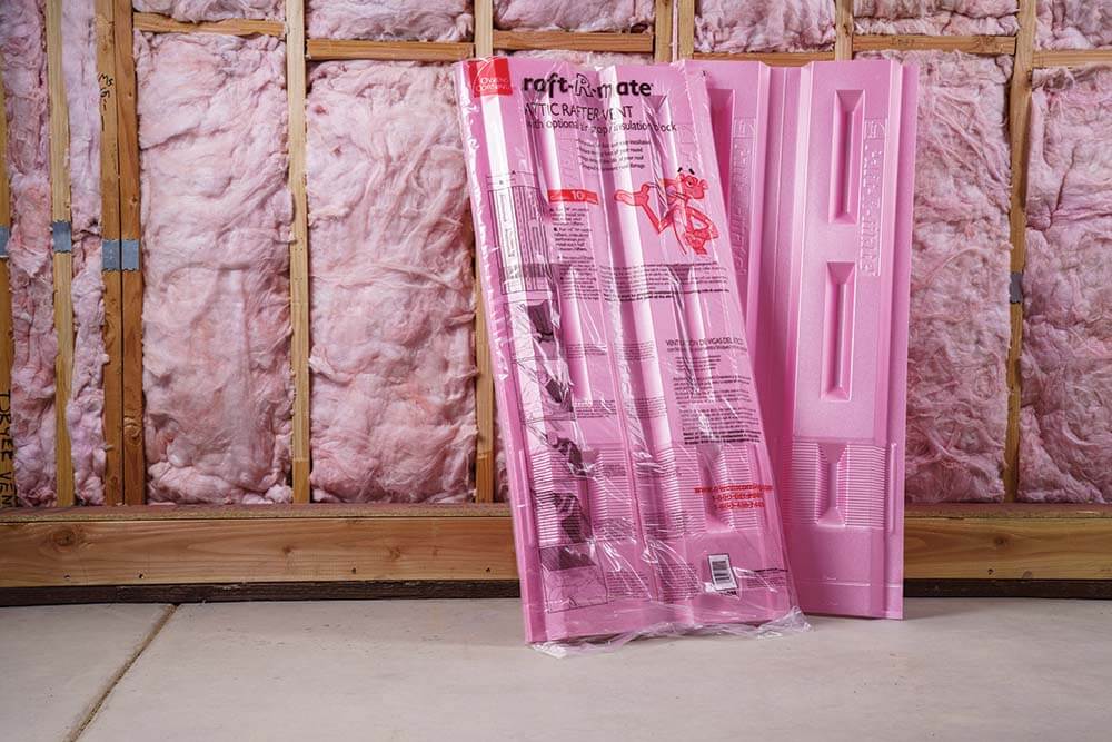 Two packs of pink Owens Corning Raft-R-Mate leaned against a wall with exposed insulation.