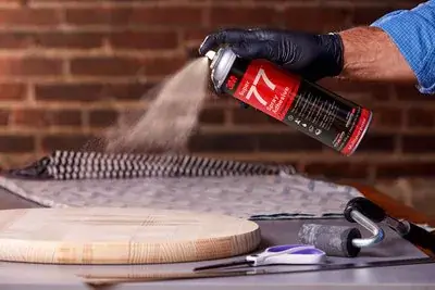 Man wearing black glove spraying 3M Super 77 Spray Adhesive to round wooden board