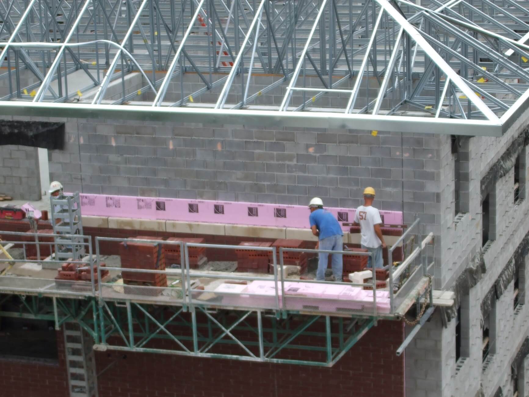 Exterior wall of commercial building with construction workers above concrete masonry