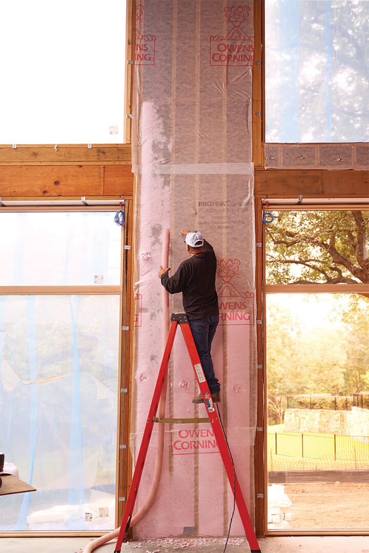 Man on ladder holding hose for spray foam insulation