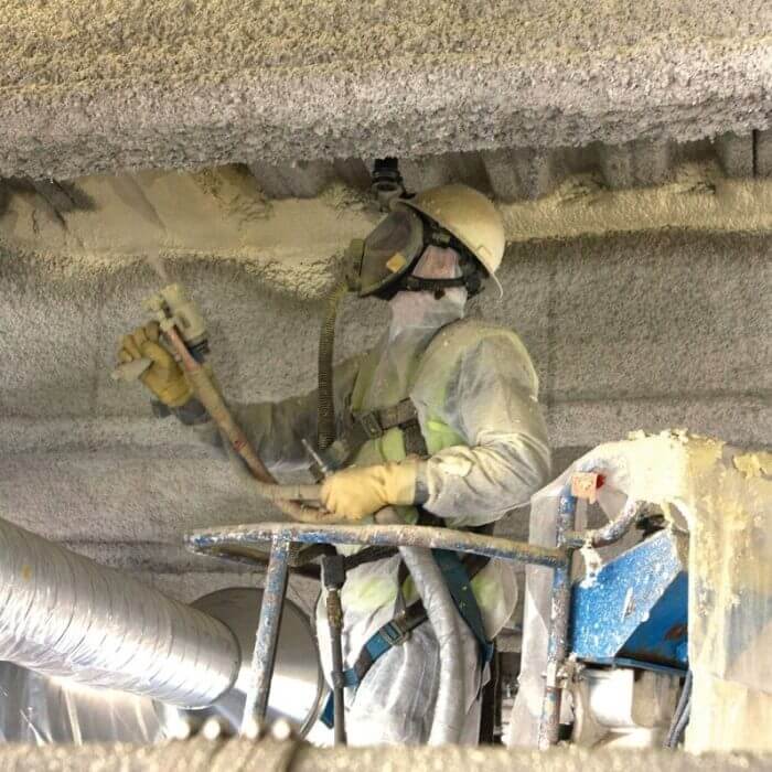 Employee in safety gear spraying foam into ceiling