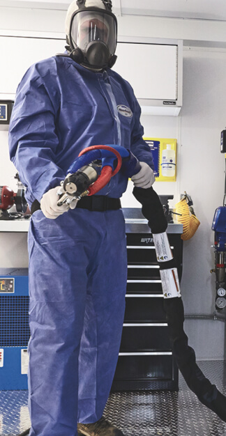 Technician wearing protective coverall, respirator mask and gloves holding an insulation hose