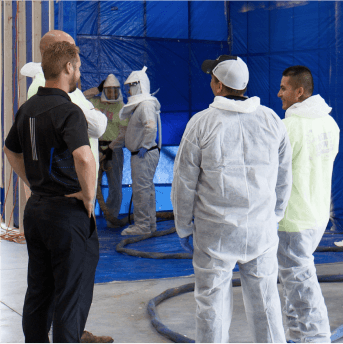 Six men standing in room with blue tarp covering wooden frame