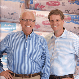 2 men posing for a picture standing in front of packaged insulation