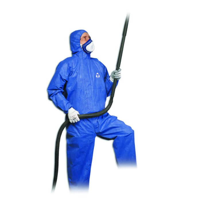 A man wearing blue protective gear, safety goggles and a mask holding a hose.