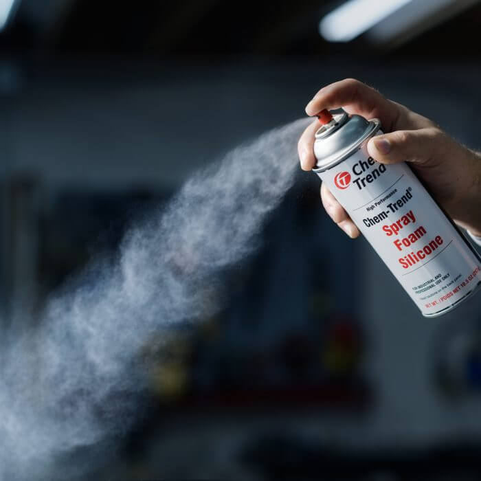 A hand spraying Chem-Trend Spray Foam Silicone from a canister.