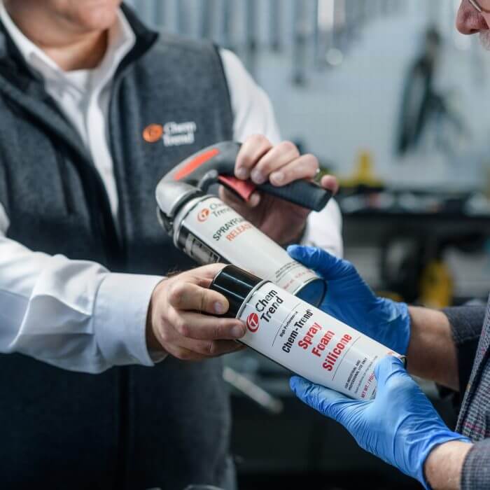 two men holding cans of Chem Trend spray foam silicone