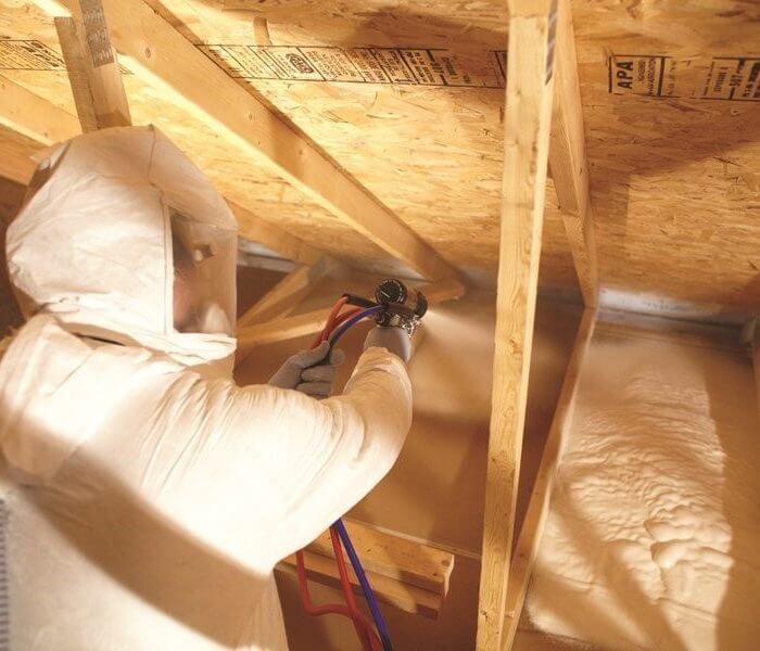 Man in protective gear spraying foam in an attic