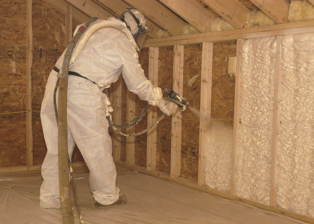 Employee in full PPE using spray foam gun to install insulation