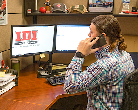 Cropped version of man answering phone in front of IDI computer