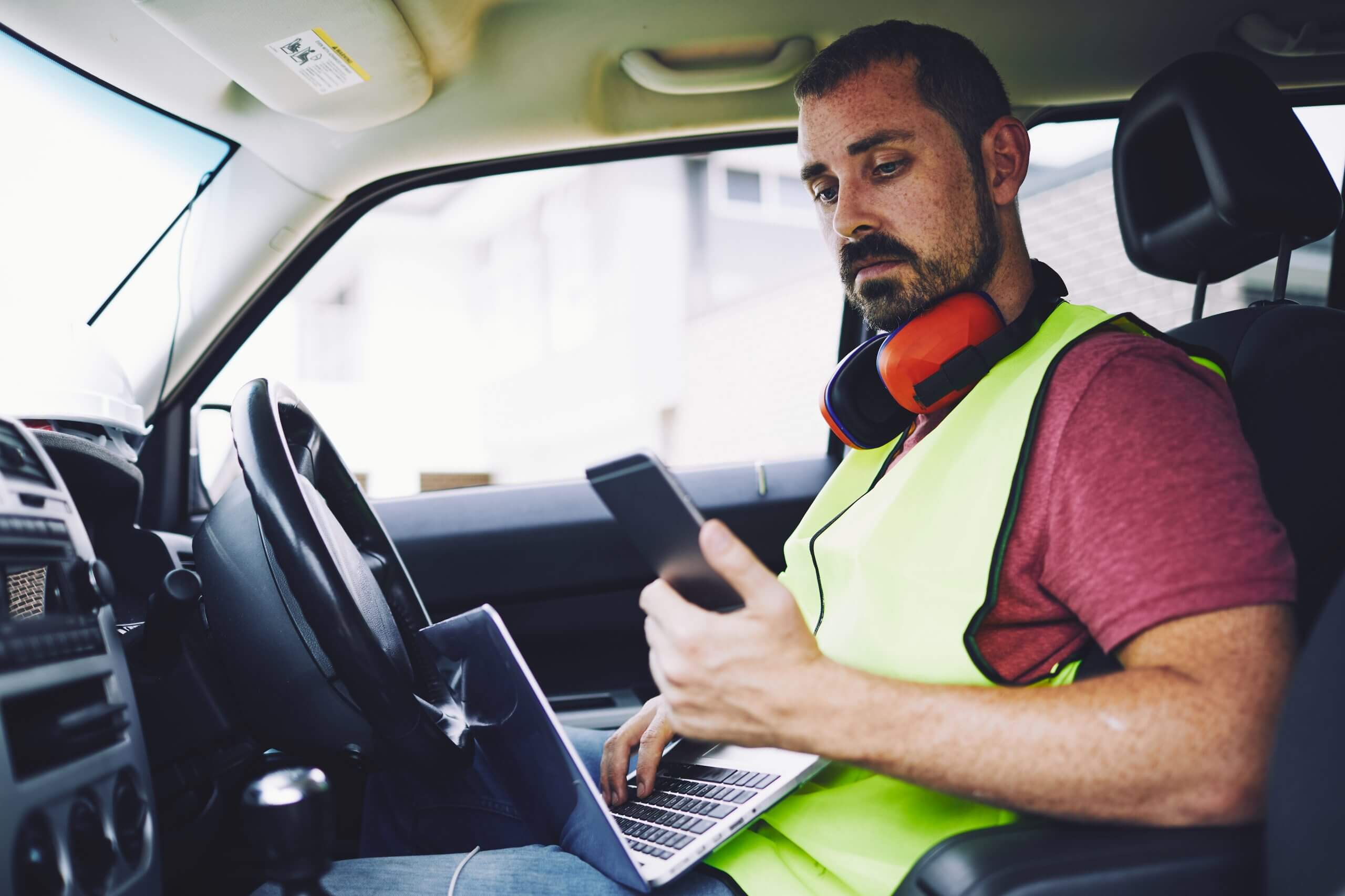 Man wearing yellow vest with laptop in work truck