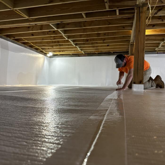 Person under a house in a crawlspace adding the Viper Crawlspace Tape to the Vapor Barrier