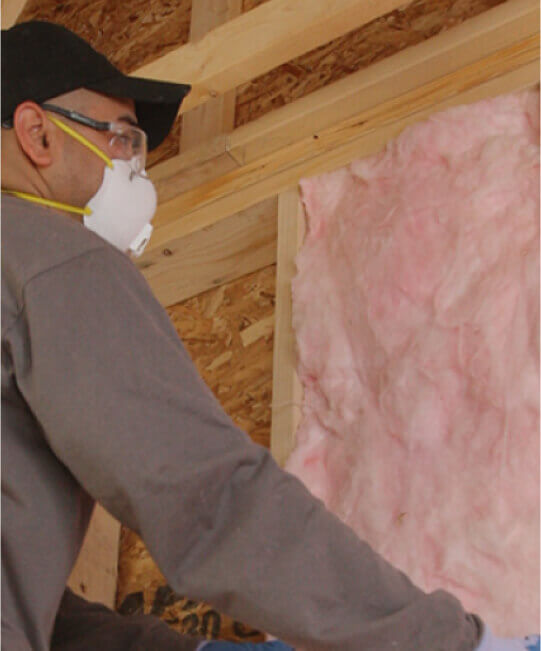 Man wearing mask and hat putting up pink insulation