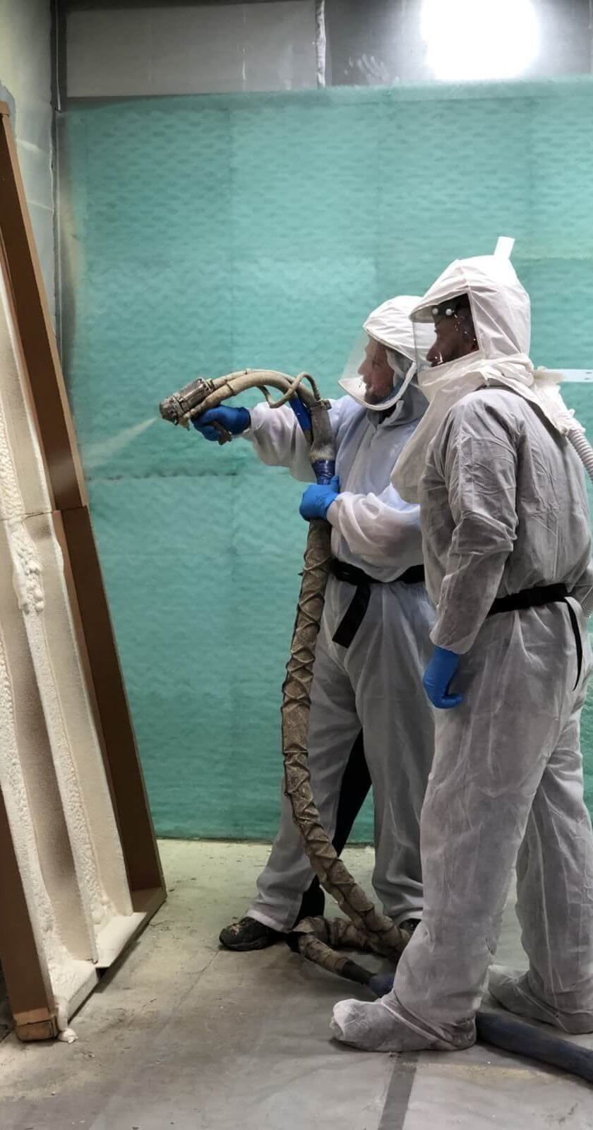 One person using a spray foam gun and another watching.